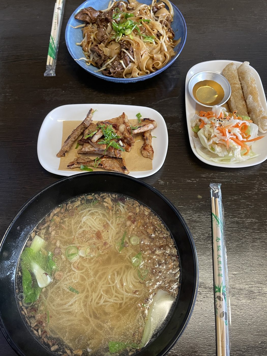 A blue bowl of wide flat rice noodles with beef, bean sprouts and spring onion