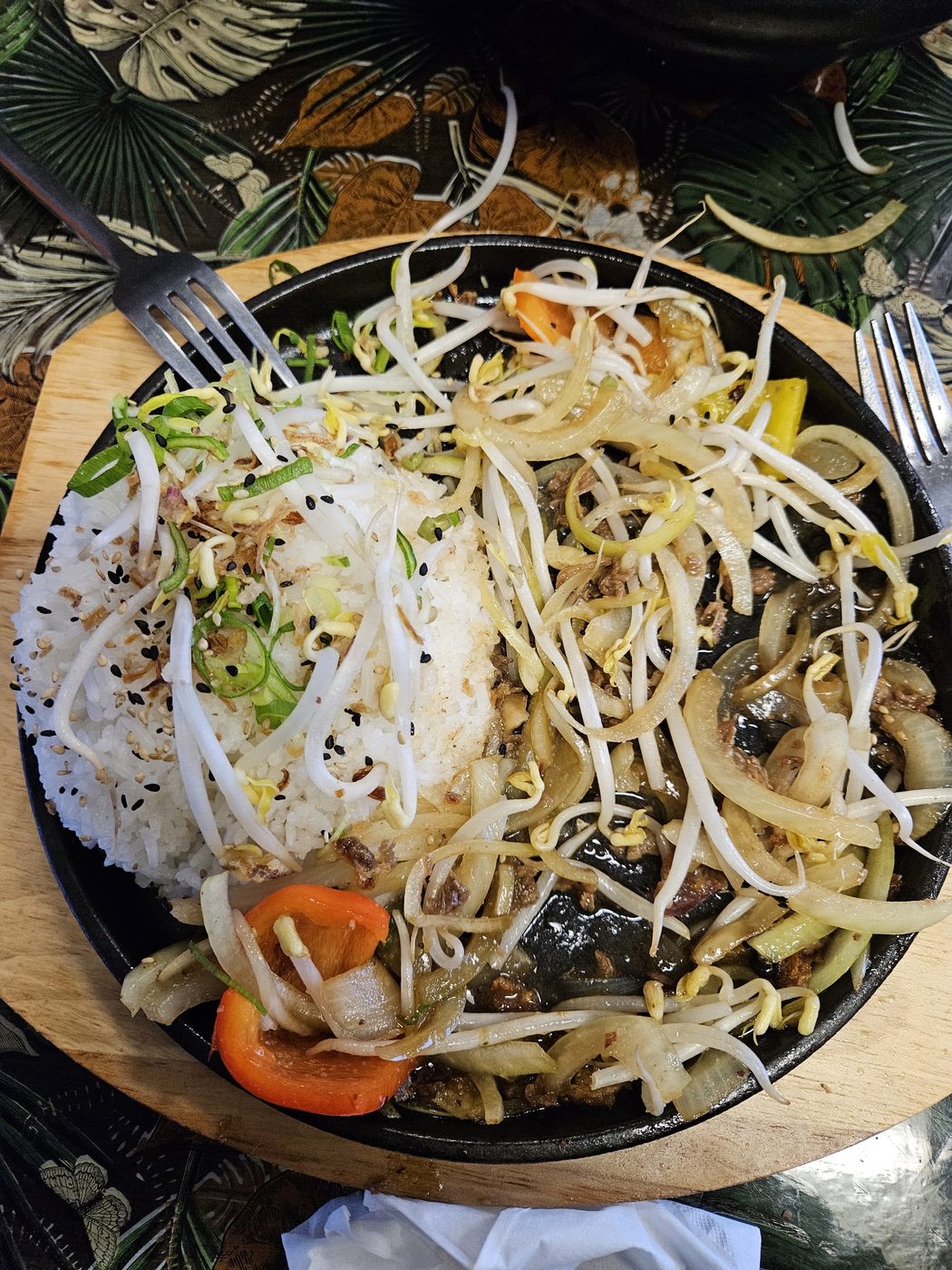 A cast-iron plate of sliced onion, capsicum and bean sprouts beside a mound of steamed rice